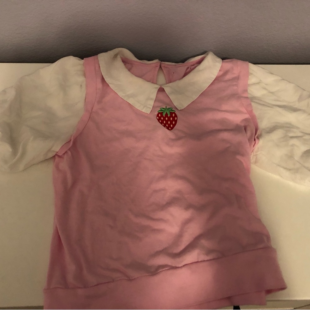 Pink and white, has a strawberry in the middle, poofy sleeves, and collared.